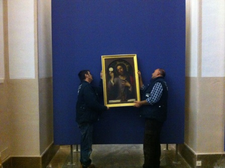 Dos operarios colgando una de las obras que se exhibirán en la exposición. FOTO: GVA